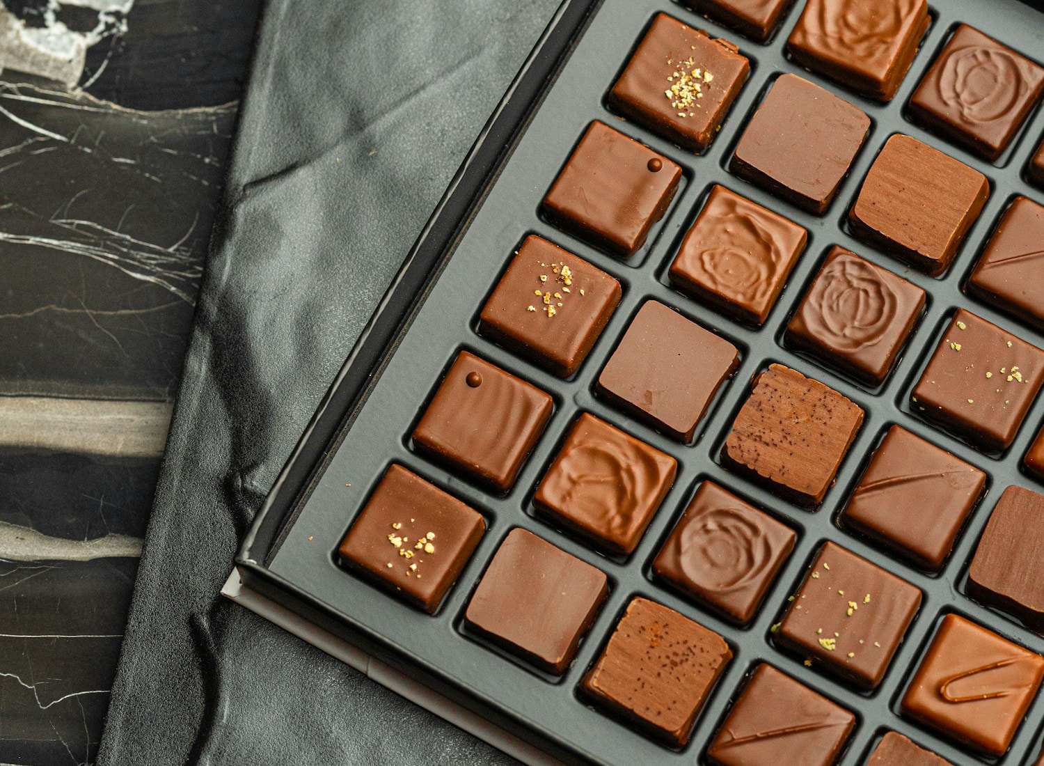 Luxury black box of artisan chocolate pralines arranged in a grid on a marble surface